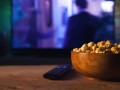 A wooden bowl of popcorn and remote control in the background the TV works. Evening cozy watching a movie or TV series at home